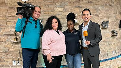 photo of news reporter and camera posing with student and faculty chair