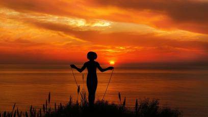 Someone standing in front of the sea at sunset who's about to jump rope