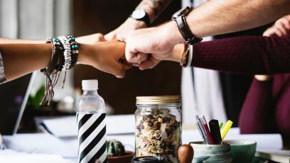 A group of co-workers bumping fists over a cluttered desk