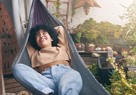 Take a Break woman in a hammock on a balcony, surrounded by plants, taking a break