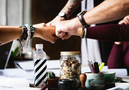 A group of co-workers bumping fists over a cluttered desk